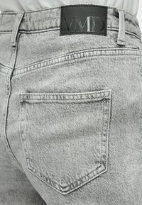 Sivi denim kavbojke z teksturirano površino, zadnjim žepom in črnim usnjenim žepnim vložkom z napisom "VMD" na pasu.