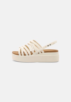 Sandales plateformes couleur crème avec plusieurs larges brides, en matériau en caoutchouc, et une semelle texturée. Le design comprend un talon bas et une bride ajustable.