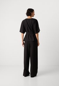 Černý peplum top s krátkými rukávy a opaskem, v kombinaci s širokými černými kalhotami, obě v texturované látce.