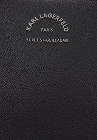Black textured leather wallet featuring embossed silver text: "KARL LAGERFELD PARIS 21 RUE ST-GUILLAUME." Minimalist design, sleek finish.