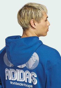 Elektrycznie niebieska bluza z kapturem z białym logo i poziomymi paskami oraz napisem na plecach. Wykonana z miękkiego bawełnianego materiału o standardowym kroju.