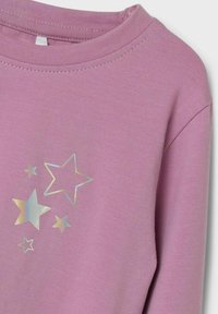 Suéter rosa con cuello redondo y mangas cortas, que presenta un estampado de estrellas iridiscentes en varios tamaños en la parte frontal.