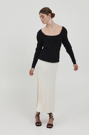 Maglione nero a maniche lunghe con scollo a barca ampio, abbinato a una gonna aderente color crema alla caviglia. Sandali neri con tacco e cinturini.