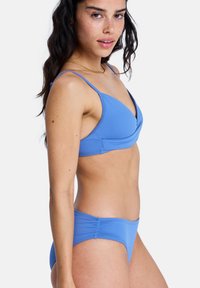 Σετ μπικίνι ανοιχτού γαλάζιου χρώματος με τοπ σε στυλ τύλιγμα, λεπτές τιράντες και σλιπ με χαμηλή μέση. Λείο ύφασμα με ελάχιστες ραφές.
