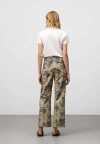 Witte top met korte mouwen en gemêleerde khaki broek met zwarte accenten. De broek heeft een ontwerp van stippen in verschillende maten. Platte zwarte sandaal.