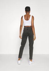 Avskuren vit linne, mörkgrå denimjeans med tapered passform och vita träningsskor. Texturerat tyg och bakfickor synliga.