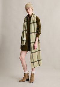 Beżowa dzianinowa czapka typu beanie, oliwkowa sukienka koszulowa z sztruksu, zielono-różowy kraciasty szalik, beżowe zamszowe botki na słupku, akcenty z fakturowanej tkaniny.