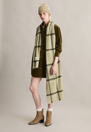 Beżowa dzianinowa czapka typu beanie, oliwkowa sukienka koszulowa z sztruksu, zielono-różowy kraciasty szalik, beżowe zamszowe botki na słupku, akcenty z fakturowanej tkaniny.