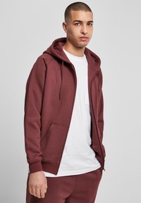 Bordo vetoki parka zadrže zavoj, prednjim džepovima i rebrastim manžetama, nosi se preko bele majice. Glatka tekstura tkanine.