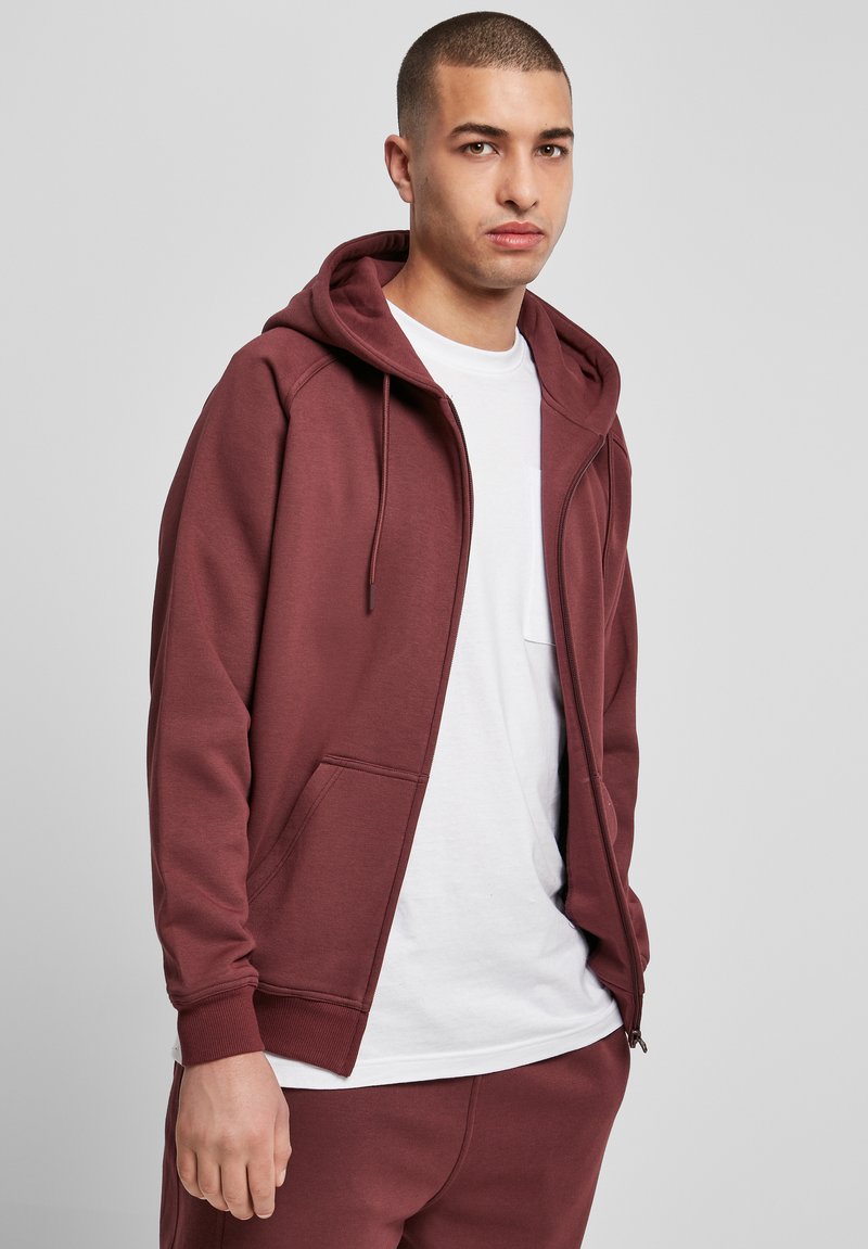 Bordo vetoki parka zadrže zavoj, prednjim džepovima i rebrastim manžetama, nosi se preko bele majice. Glatka tekstura tkanine.