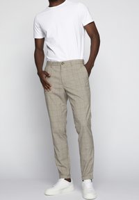 Vaaleat ruudulliset housut kapealla leikkauksella, joissa on yksi nappi kiinnityksessä, sivutaskut, ja joita käytetään yksinkertaisen valkoisen t-paidan ja valkoisten kenkien kanssa.