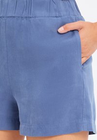 Blauwe shorts van een textuurstof, met een elastische tailleband en zijzakken. Heeft een rechte snit met een nette afwerking aan de zoom.