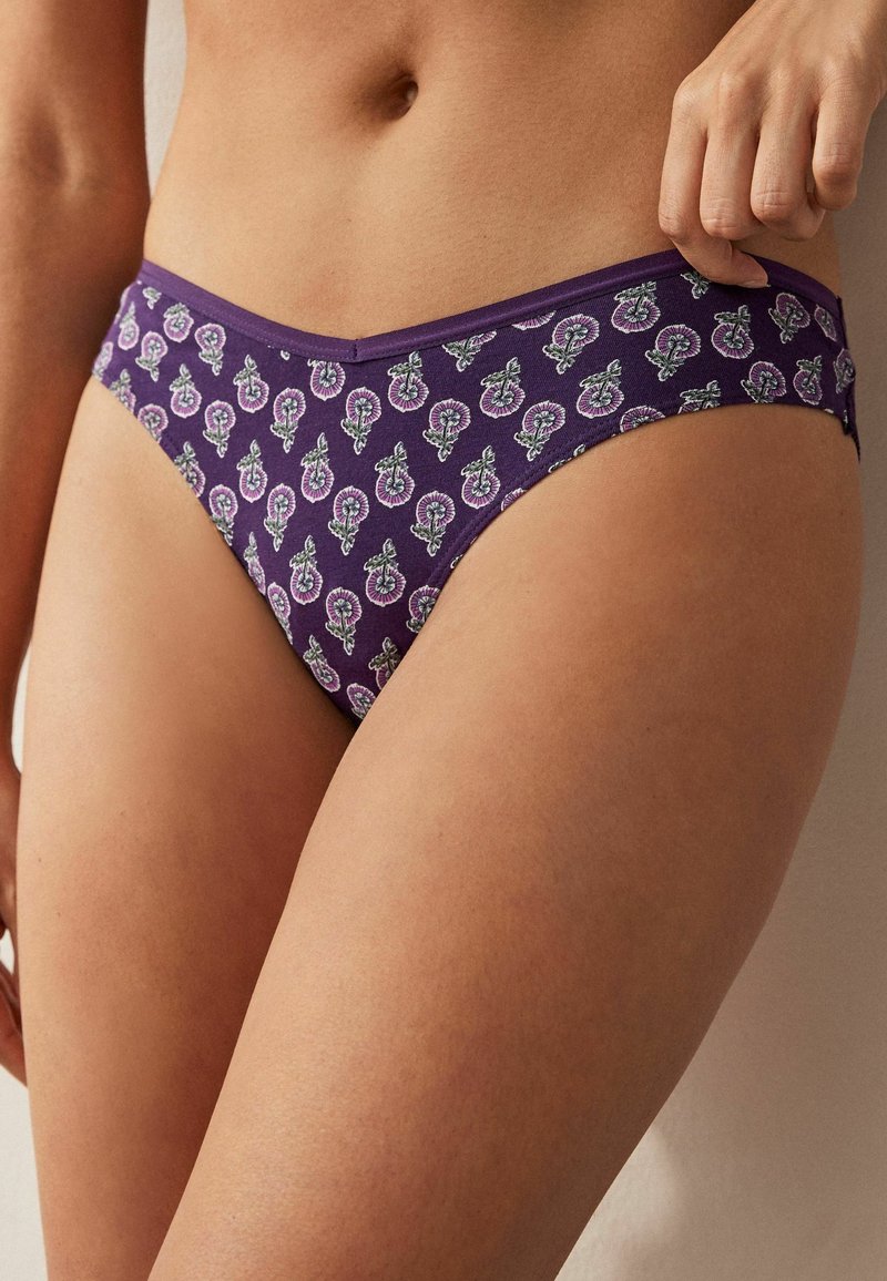 Paarse katoenen bikini met bloemenpatronen in roze en groen. Heeft een lage taille en een elastische tailleband voor comfort.