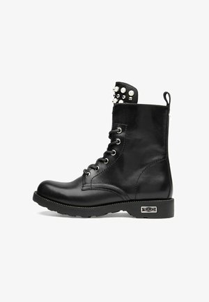 Bottines en cuir noir avec un bout rond, lacets à l'avant, accents métalliques et détails cloutés en haut. Semelle en caoutchouc robuste.