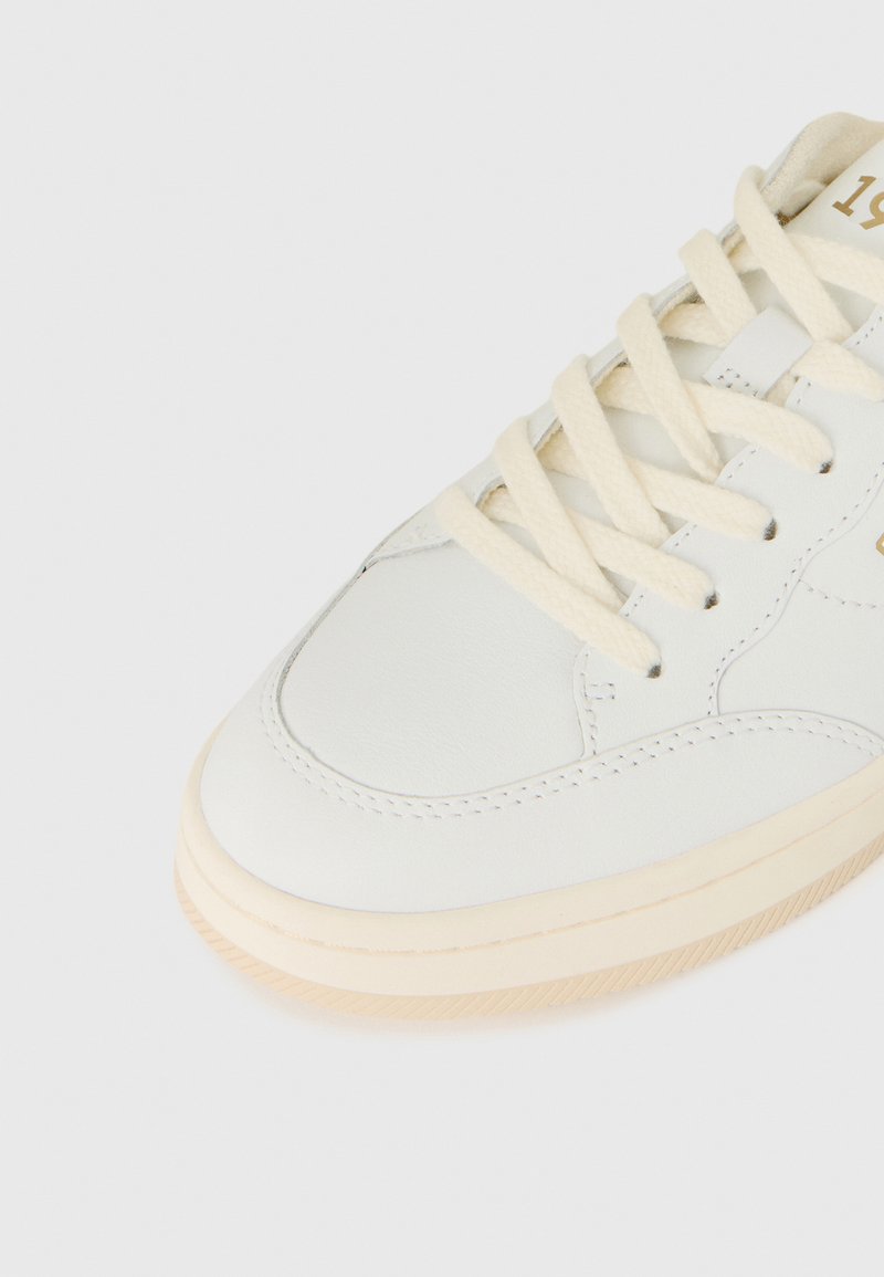 Weiße Leder-Sneaker mit cremefarbenen Schnürsenkeln, runder Zehenpartie und cremefarbener Gummisohle. Verfügt über Nähdetails und ein Logo in der Nähe der Schnürsenkel.