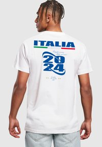 Valge puuvillane T-särk, millel on suur sinine "2024" kujundus, sinine "ITALIA" ja Itaalia lipu aktsendid. Prinditud tekst ja graafilised detailid seljal.