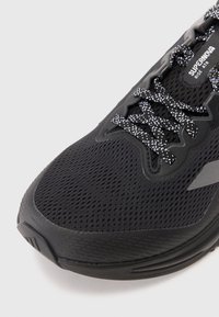 Baskets noires avec tige en mesh respirant, lacets à motifs et subtils accents gris. Présente une semelle en caoutchouc texturé pour l'adhérence.