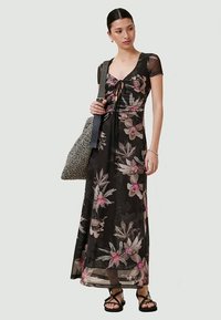 Vestido maxi preto com estampado floral, com mangas curtas, um cordão na frente e uma silhueta fluida; combinado com uma bolsa texturizada.