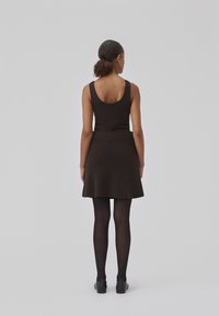 Svart strikket tank topp kombinert med en utsvingt brun skjørt. Outfiten kompletteres av svarte strømpebukser og ankelstøvler. Visning fra bak.