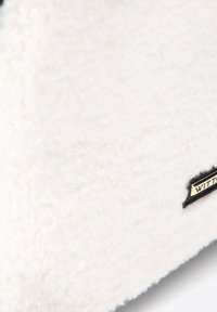 Bílá nadýchaná tkanina s měkkou texturou, na okraji s černou etiketou se zlatým písmem. Jednoduchý a minimalistický design.