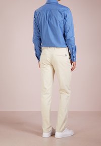 Ljusblå skjorta med prickar, långärmad och med knäppning vid kragen, ihop med beige chinos och vita sneakers. Bakifrån av outfiten.