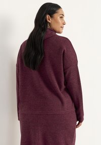 Bordeaux gebreide trui met een hoge kraag en een dropped shoulder, voorzien van een zachte textuur en een ontspannen pasvorm. Minimalistisch ontwerp.