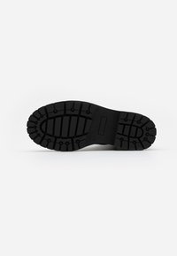 Black rubber shoe sole with deep grooves for traction, featuring a textured surface and rectangular branding area.