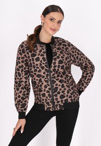 Giacca bomber in stampa leopardata beige e nera, con chiusura a zip, polsini e orlo a coste, dal taglio comodo. Sotto, una maglietta nera e leggings.