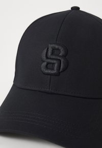 Mustapohjainen baseball-lippis, jossa on rakennettu muotoilu, ja siinä on teksturoitu, kohokuvioitu logo. Materiaali on sileä, ja siinä on näkyviä ompeluyksityiskohtia.