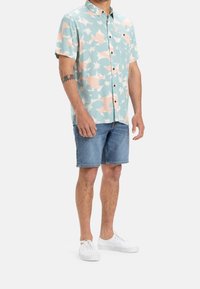 Košile s krátkými rukávy na knoflíky s jemným modro-růžovým květinovým vzorem, doplněná o džínové šortky a bílé tenisky.