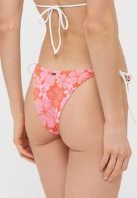 Bas de bikini en corail avec des motifs floraux roses, liens sur les côtés ajustables et texture lisse. Conçu pour un ajustement taille basse.
