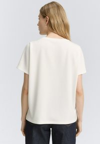 Haut blanc à manches courtes avec un col rond et une texture douce. Conçu avec une coupe décontractée et une finition droite à l'ourlet. Porté avec un jean foncé.