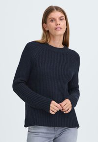 Pull en tricot bleu marine avec des manches longues côtelées, un col rond et un motif texturé ; présente une coupe décontractée avec des fentes sur les côtés à l'ourlet.