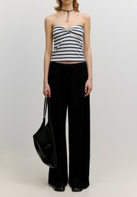 Gestreepte bustiertop in crème en marineblauw, gecombineerd met zwarte wijde pantalon. Model houdt een zwart leren totebag vast. Eenvoudig, aansluitend ontwerp.