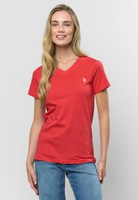 Sarkanais V-veida krekls, izgatavots no mīkstas kokvilnas, ar īsām piedurknēm un mazu logo kreisajā krūtī. Kombinēts ar ziliem džinsiem.