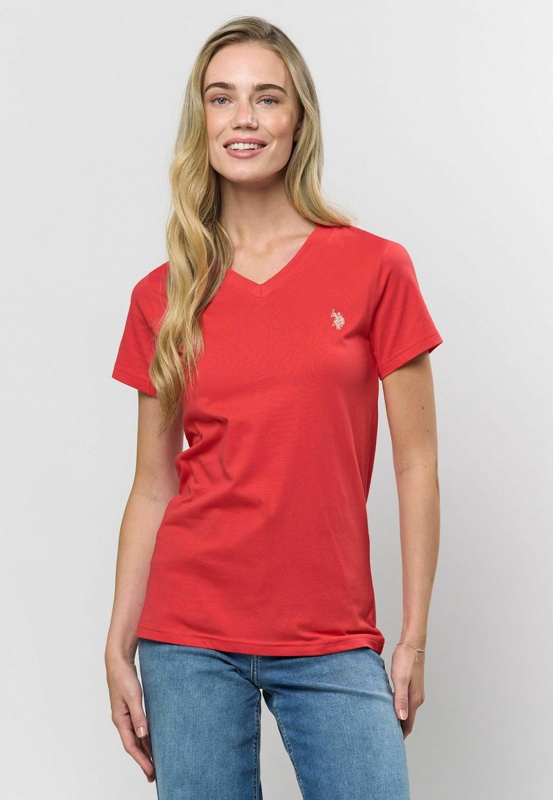 Sarkanais V-veida krekls, izgatavots no mīkstas kokvilnas, ar īsām piedurknēm un mazu logo kreisajā krūtī. Kombinēts ar ziliem džinsiem.