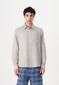 Beige karierte Hemd, mit Knopfverschluss, lange Ärmel, einzelnes Brusttasche, aus leichtem Stoff. Kombiniert mit blauen gemusterten Hosen.