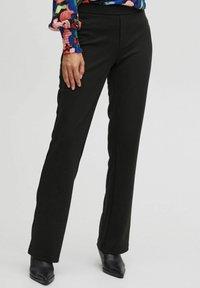 Black, straight-leg trousers made of stretchy fabric. Features a smooth texture and a fitted waistband, paired with black pointed-toe heels.