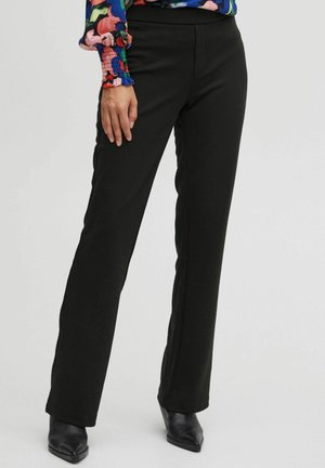 Black, straight-leg trousers made of stretchy fabric. Features a smooth texture and a fitted waistband, paired with black pointed-toe heels.