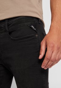 Svarta denim jeans med slim fit, med en framficka, subtila sömmar och en logotyp på bakfickan. Slät textur.