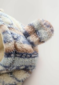 Blød fleece vinterhat med pom-pom, prydet med et flerfarvet abstrakt mønster i beige, blå og hvide nuancer.