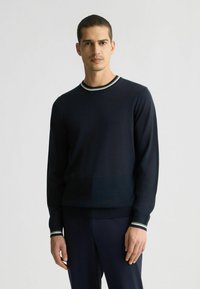 Suéter de punto azul marino con mangas largas, escote redondo y ribetes blancos contrastantes en el cuello y los puños. Textura suave.