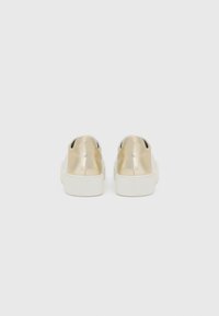 Metallisch goldene Rückenteile mit einer weißen Gummisohle. Glatte Oberfläche und minimalistisches Design, ohne sichtbare Schnürsenkel oder Akzente.