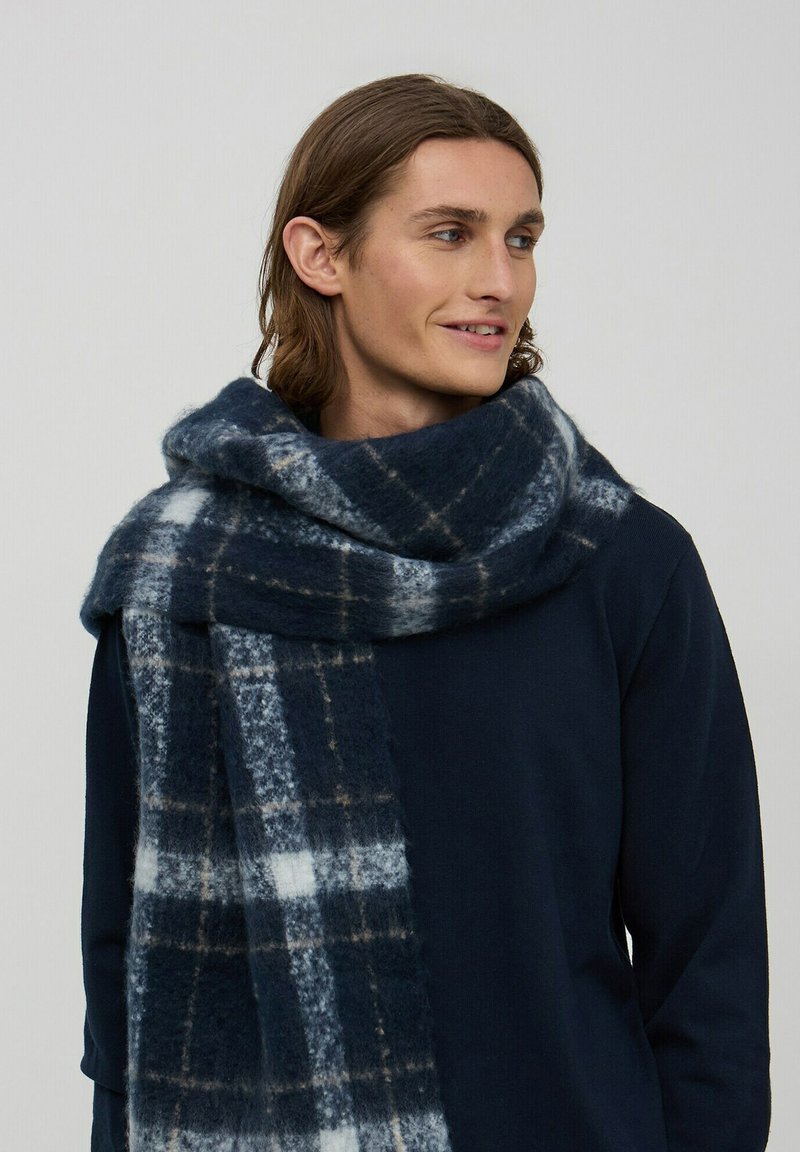 Granatowa szal w kratę wykonany z miękkiej mieszanki wełny, z wzorem w białe i beżowe kraty. Gruby i długi, o przytulnej fakturze.