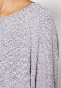 Maglione a maglia grigio chiaro con texture a coste, scollatura ampia e cuciture delle spalle abbassate. Il tessuto appare morbido e traspirante.