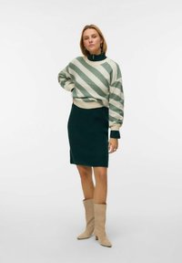 Sweter dzianinowy w białe i zielone paski z wysokim kołnierzem, w poł�ączeniu z ciemnozieloną mini spódnicą i beżowymi kozakami do kolan.