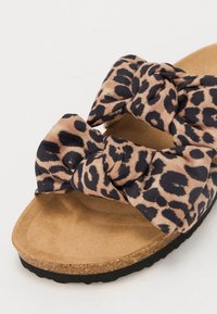 Leopard-print slide sandal with a large, knotted bow on a soft, faux suede upper, and a cushioned, tan-colored cork footbed. Black textured sole.