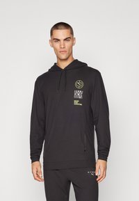 Svart hettegenser med lange ermer har snor, sideslisser og trykte logoaksenter i hvitt og neongrønt. Glatt stofftekstur.