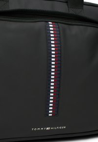 Borsa da viaggio in tessuto nero con una striscia verticale nei colori rosso, bianco e blu navy; dettaglio del logo in oro nella parte inferiore.