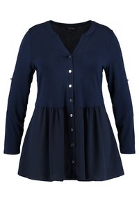 Cardigan à manches longues bleu marine avec fermeture à boutons sur le devant, encolure arrondie, et ourlet évasé à design superposé. Texture de tissu lisse.